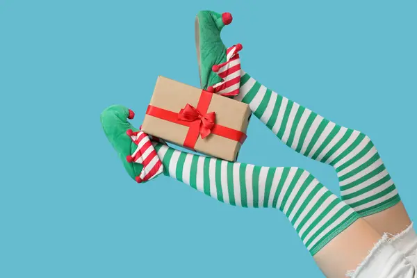 stock image Legs of young woman in elf shoes with gift box on blue background