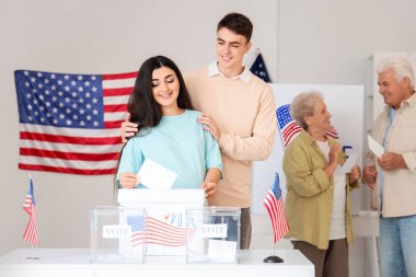 Oy kullanma merkezindeki Amerikan bayrağıyla oy sandığının yanında genç hamile bir çift oy kullanıyor.