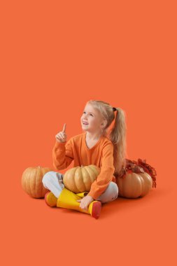 Balkabaklı şirin kız turuncu arka planda bir şeye bakıyor.
