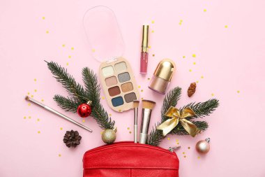 Pembe arka planda köknar dalları, kozmetik poşeti ve makyaj ürünleriyle güzel Noel süslemeleri