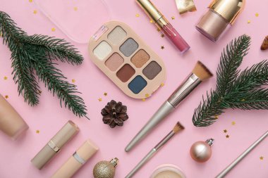 Köknar dallarıyla güzel Noel süslemeleri ve pembe arka planda farklı makyaj ürünleri.