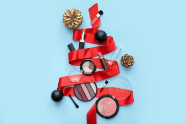 Makyaj ürünlerinden yapılmış Noel ağacı, süslemeler ve mavi arka planda kurdele