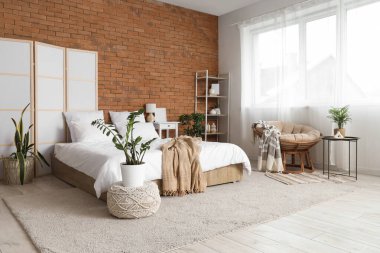 Konforlu yatağı, çiçekleri ve beyaz katlı ekranı olan aydınlık yatak odasının içi.