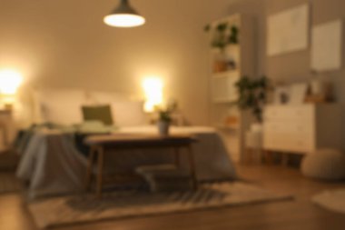 Karanlık yatak odasının bulanık manzarası, rahat yatağı ve parlak lambaları.