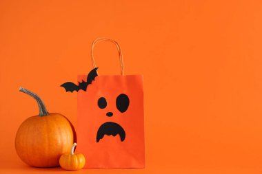 Cadılar Bayramı alışveriş çantası, balkabağı ve turuncu arka planda kağıt yarasa.