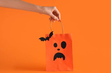 Cadılar Bayramı alışveriş çantası ve turuncu arka planda kağıt yarasa taşıyan bir kadın.
