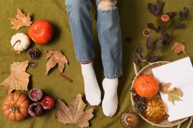 Sonbahar yaprakları, mumlar ve arka planda yeşil ekoseli balkabakları olan kadın çorapları.