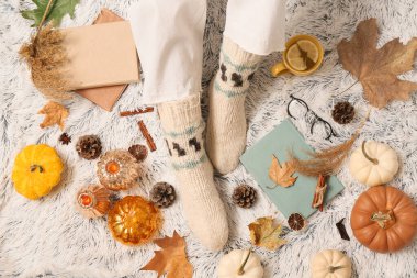 Sonbahar yaprakları, balkabakları ve arka plan olarak beyaz ekoseli bir fincan çay ile sıcak çoraplar içindeki kadın bacakları.