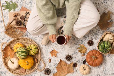 Sonbahar yaprakları, balkabakları ve arka plan olarak beyaz ekoseli bir fincan çay ile sıcak çoraplar içindeki kadın bacakları.
