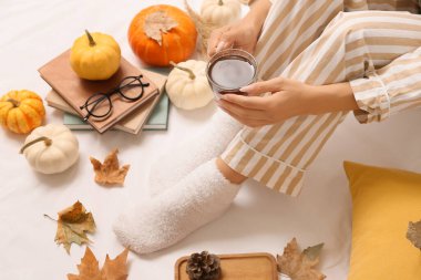 Sonbahar yaprakları, kitaplar, bir fincan kahve ve yatağın üzerinde balkabağı olan kadın çorapları.