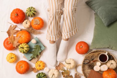 Sonbahar yapraklı, sıcak çoraplı kadın bacakları, yatakta bir fincan kahve ve balkabağı.