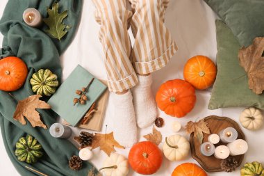 Sonbahar yaprakları, kitaplar, mumlar ve balkabaklarıyla sıcak çoraplar içinde kadın bacakları.