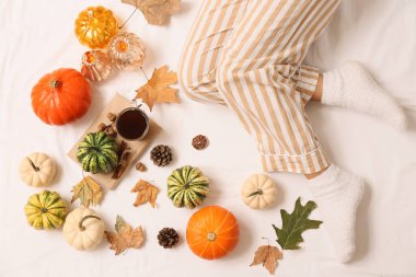 Sonbahar yapraklı, sıcak çoraplı kadın bacakları, yatakta bir fincan çay ve balkabağı.