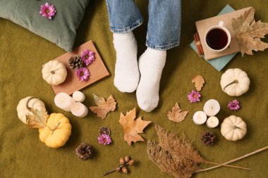 Sonbahar yaprakları, balkabakları, mumlar ve arka planda yeşil ekoseli bir fincan çay olan kadın çorapları.