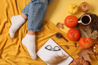 Sonbahar yapraklı, balkabaklı, ekoseli ve sarı arka planda çay fincanlı sıcak çoraplı kadın bacakları.