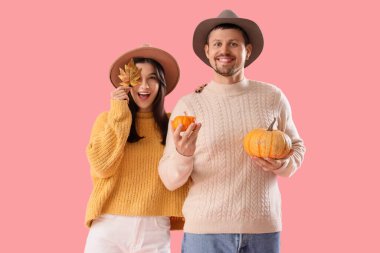 Sonbahar kıyafetleri içinde pembe arka planda balkabakları olan genç bir çift.