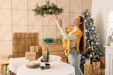 Yemek odasında Noel çelengi asan genç bir kadın.