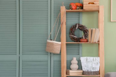 Yeşil duvarın yanında balkabağı, kitap ve dekor olan raf ünitesi.