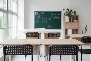 Okul sıraları olan boş sınıfın içi ve karatahtadaki okula geri dönüş metni