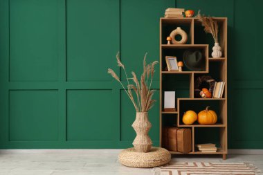 Yeşil duvarın yanında balkabağı, kitap ve dekor olan raf ünitesi.