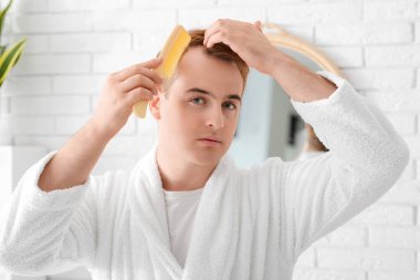 Saç dökülme sorunu olan genç kızıl saçlı adam banyoda tarama yapıyor.