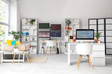 Masaları, raf üniteleri ve kanepesi olan ışık programcıları ofisinin içinde.