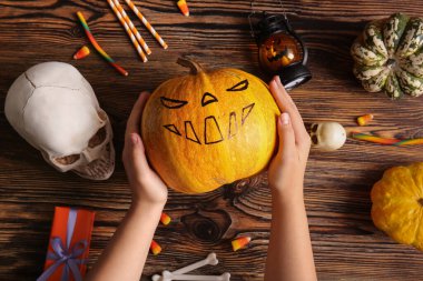 Cadılar Bayramı balkabaklı kadın elleri, hediye kutusu ve kahverengi ahşap arka planda süslemeler.