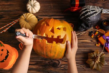 Kahverengi ahşap arka planda Cadılar Bayramı için balkabağı oyan dekorasyonlu bir kadın.