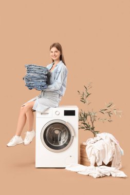 Çamaşır makinesinde bej arka planda oturan kot pantolonlu genç kadın.