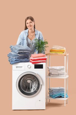 Çamaşır makinesinde bej arka planda çamaşır yığını olan genç bir kadın.