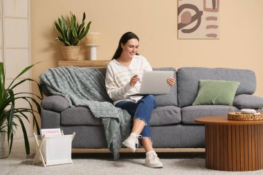 Evde kanepede dizüstü bilgisayar kullanan genç kadın