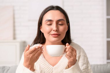 Evde bir fincan kahveyle genç bir kadın, yakın plan.