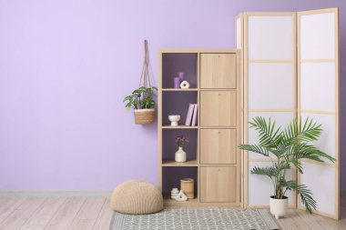 Ev dekorlu raf ünitesi, ev çiçekleri ve şık bir odada menekşe duvarının yanında katlanan ekran.