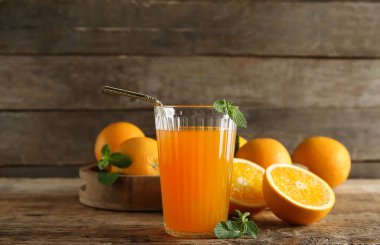 Bir bardak taze portakal suyu, nane ve ahşap arka planda meyveler.