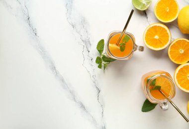 Mason kavanozları dolusu taze portakal suyu ve beyaz arka planda farklı narenciye meyveleri.