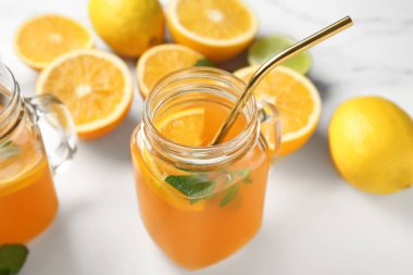 Mason kavanozları dolusu taze portakal suyu ve beyaz arka planda farklı narenciye meyveleri.