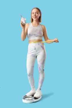 Kilo terazisinde chia tohumu pudingi olan genç bir kadın mavi arka planda.