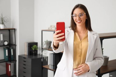 Ofiste cep telefonu görüntülü sohbet yapan genç bir iş kadını.