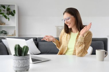 Evdeki masada dizüstü bilgisayarla görüntülü sohbet eden mutlu genç kadın.