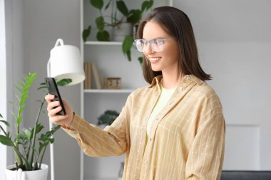 Cep telefonlu genç bir kadın evde görüntülü sohbet ediyor.