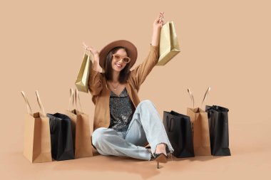 Bej arka planda oturan alışveriş çantalı genç bir kadın. Kara Cuma İndirimi