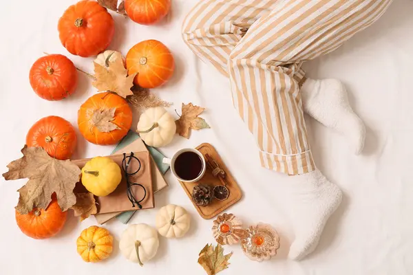 Sonbahar yaprakları, kitaplar, bir fincan kahve ve yatağın üzerinde balkabağı olan kadın çorapları.