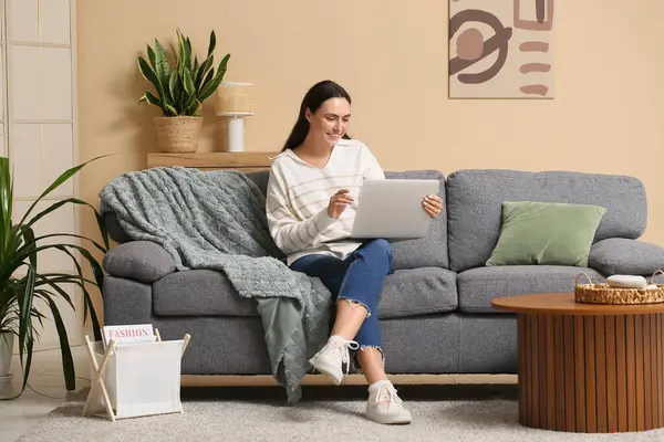 Evde kanepede dizüstü bilgisayar kullanan genç kadın