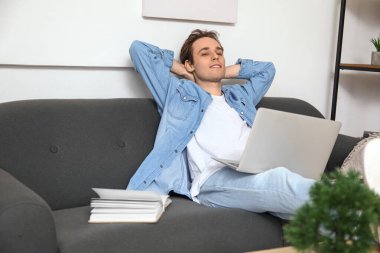 Evdeki kanepede dizüstü bilgisayarı olan serbest çalışan bir erkek.