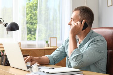 Ofiste cep telefonuyla konuşan olgun bir erkek serbest yazar.