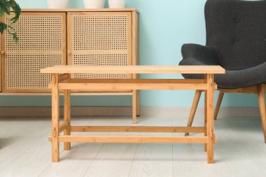 Mavi duvarın yanında koltuğu ve şifoniyeri olan kahve masası.