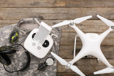 Modern kuadkopter, uzaktan kumanda, pusula, saat, kulaklık ve askeri üniforma ahşap arka planda.