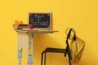 Modern okul masası, kırtasiye ve karatahta. Sarı duvarın yanındaki odada okula dönüş yazısı var.