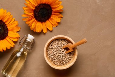 Ayçiçekleri, tohumlu kase ve kahverengi arka planda bir şişe yağ.