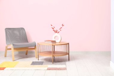 Grey armchair, coffee table and stylish rug near pink wall